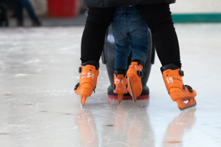An adult and a child ice skating with an aide on an ice rink. 