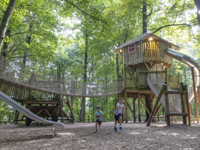 two children running through an outdoor playground with a treehouse