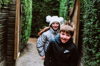 Two kids running through the maze with winter hats on
