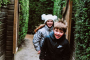 Two kids running through the maze with winter hats on