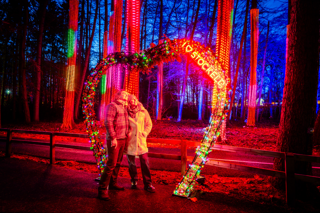  A couple standing beneath an illuminated love heart with an ‘I love Stockeld’ sign outside in the Enchanted Forest. 