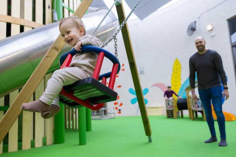 father pushing child in playhive at stockeld park