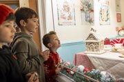 Three children looking through a window into a Christmas kitchen scene, at a gingerbread house.