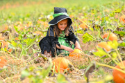 girl in a green and black witches costume in a pumpkin patch choosing a pumpkin