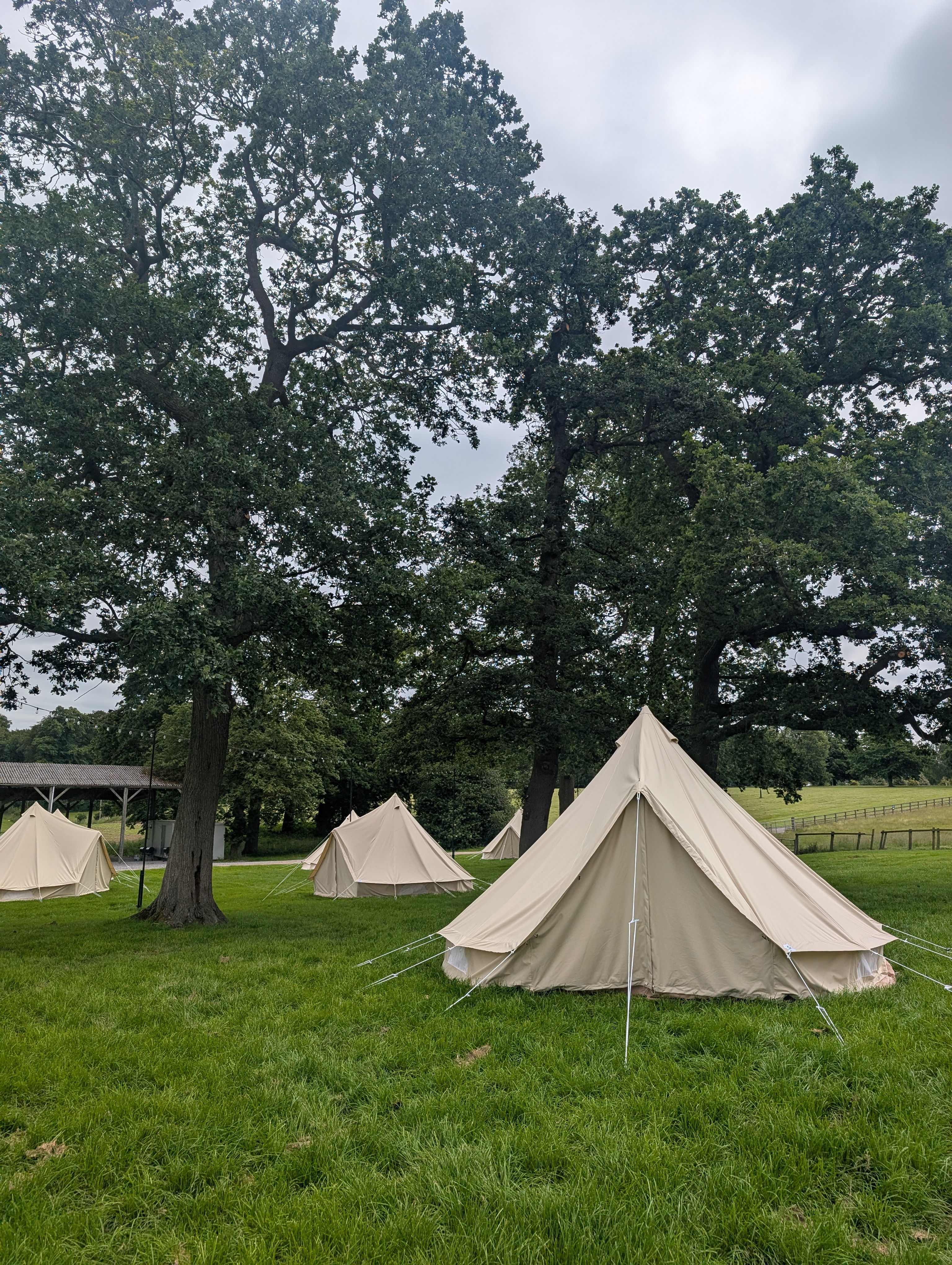 A White Bell Tent In A Field With Trees And Other Tents In The Background