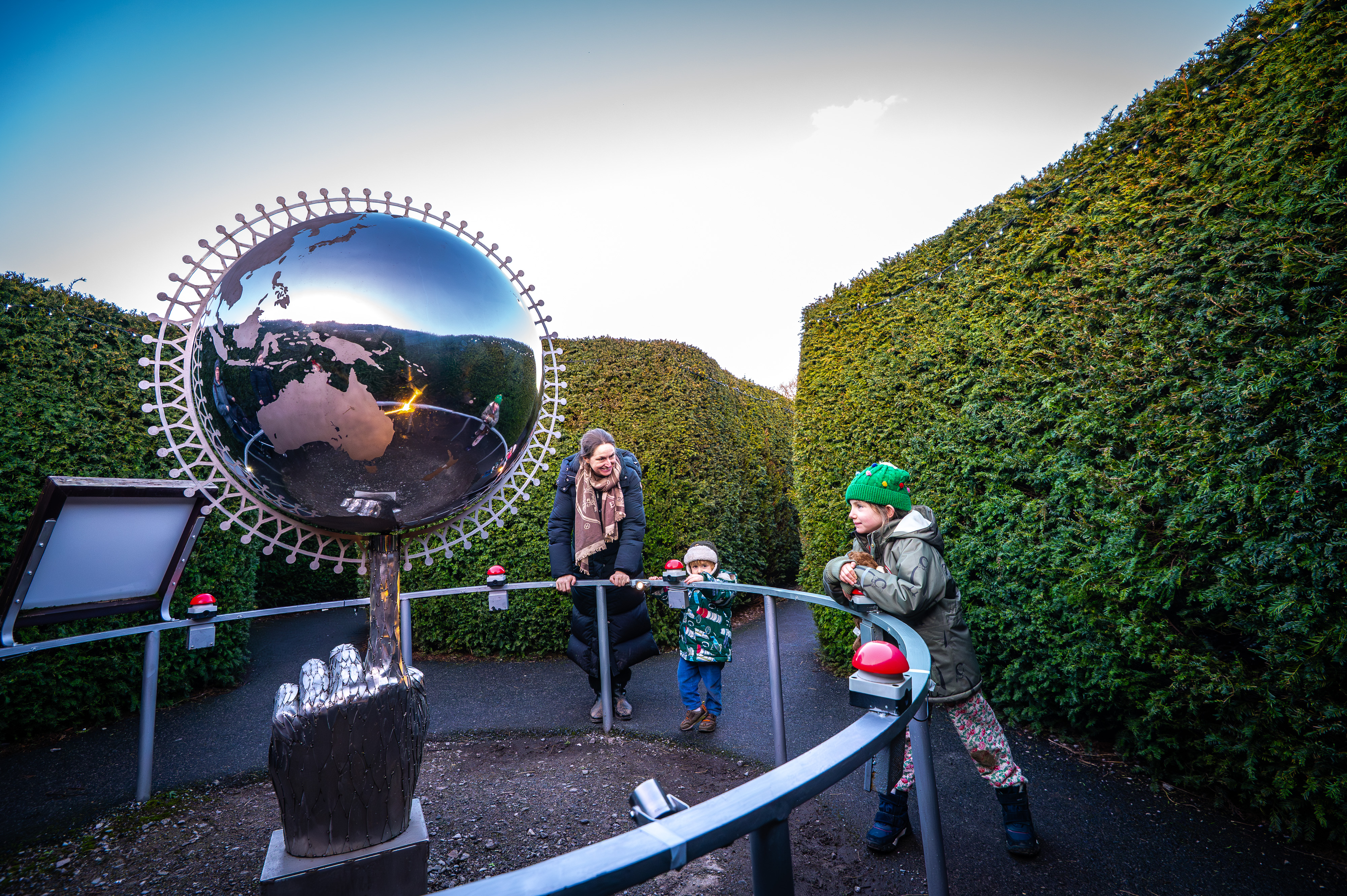 family look at silver globe sculpture in a maze