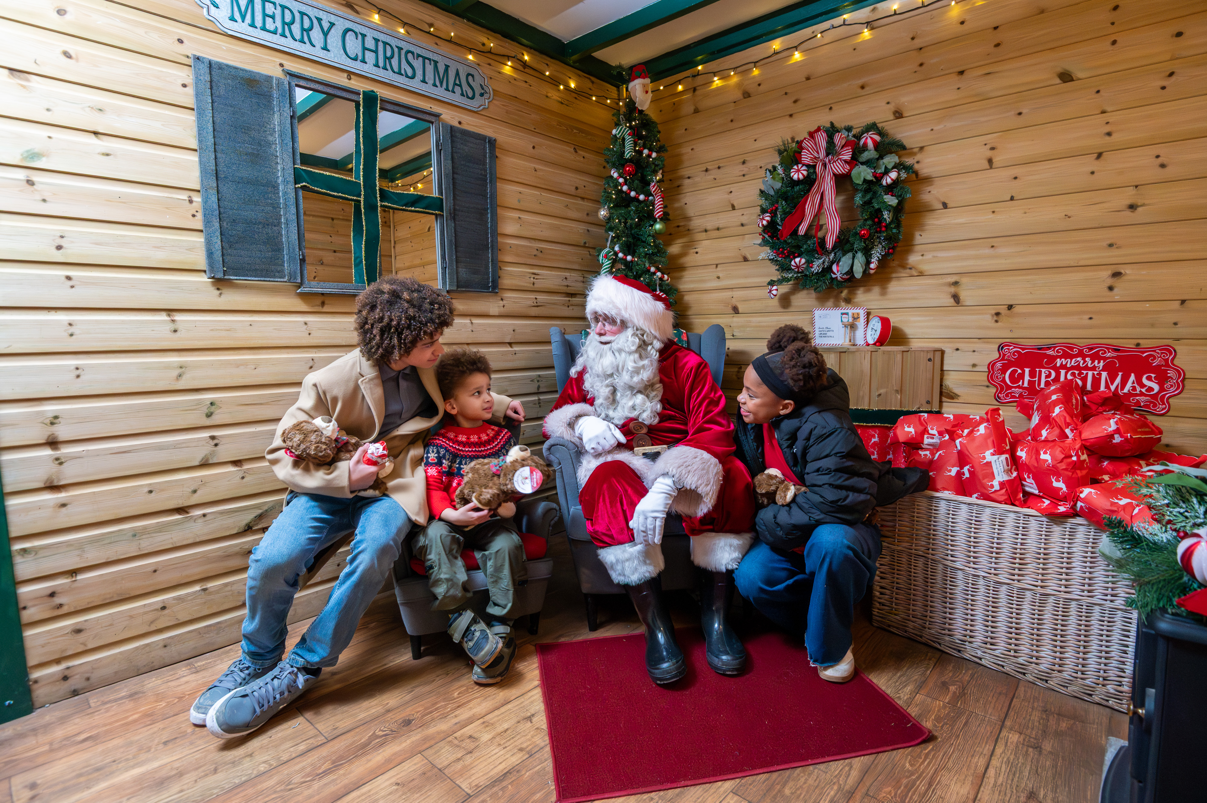 three children hold teddy bears as they talk to santa in his grotto