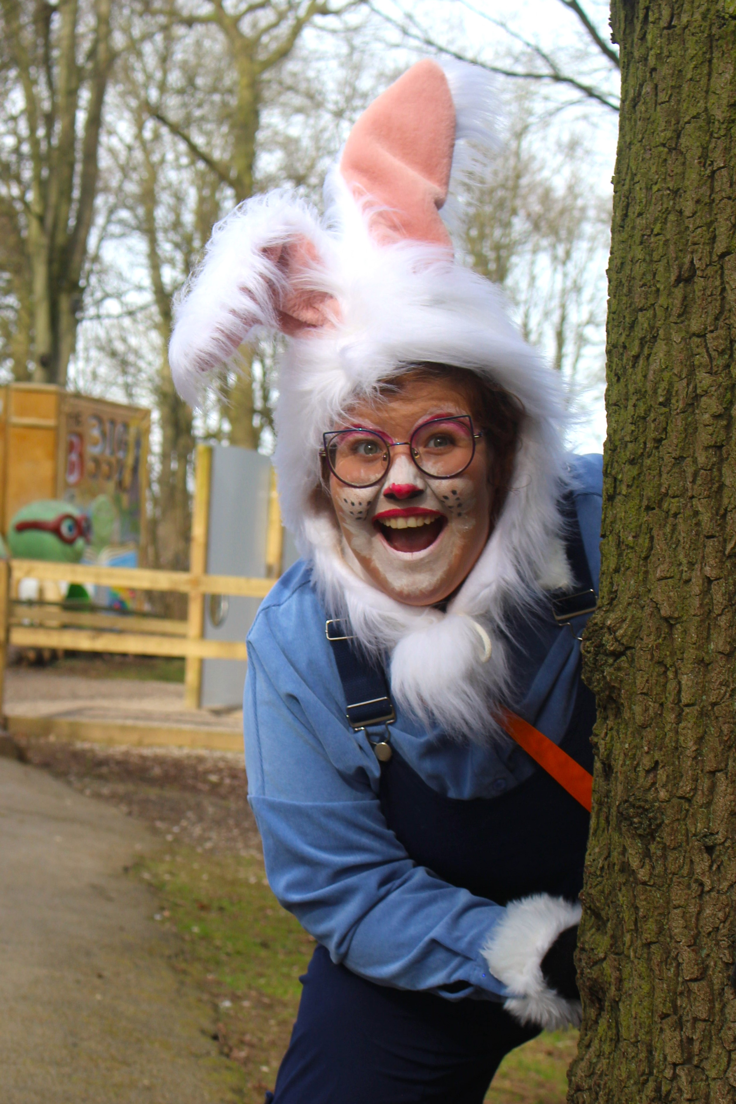 rabbit character smiling with white fur and dungarees from behind tree