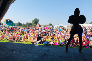 A performer on stage in front of a large crowd on a summer's day at Stockeld Park.