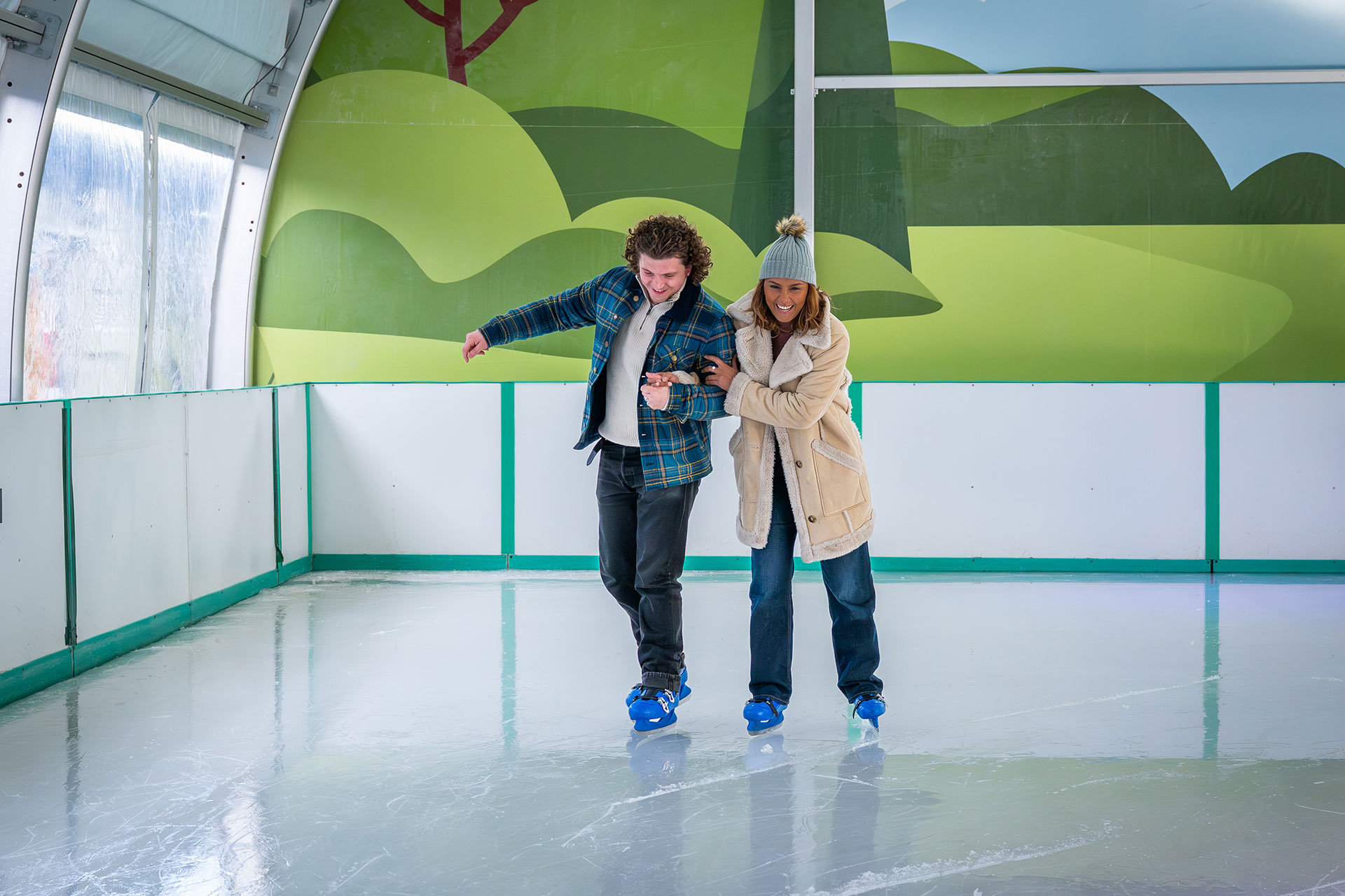 couple in winter coats ice skating on a covered ice rink