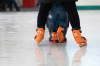 close up shots of orange ice skates as parent and child skate together on ice rink