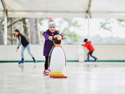 A young girl ice skating with a penguin skating aid