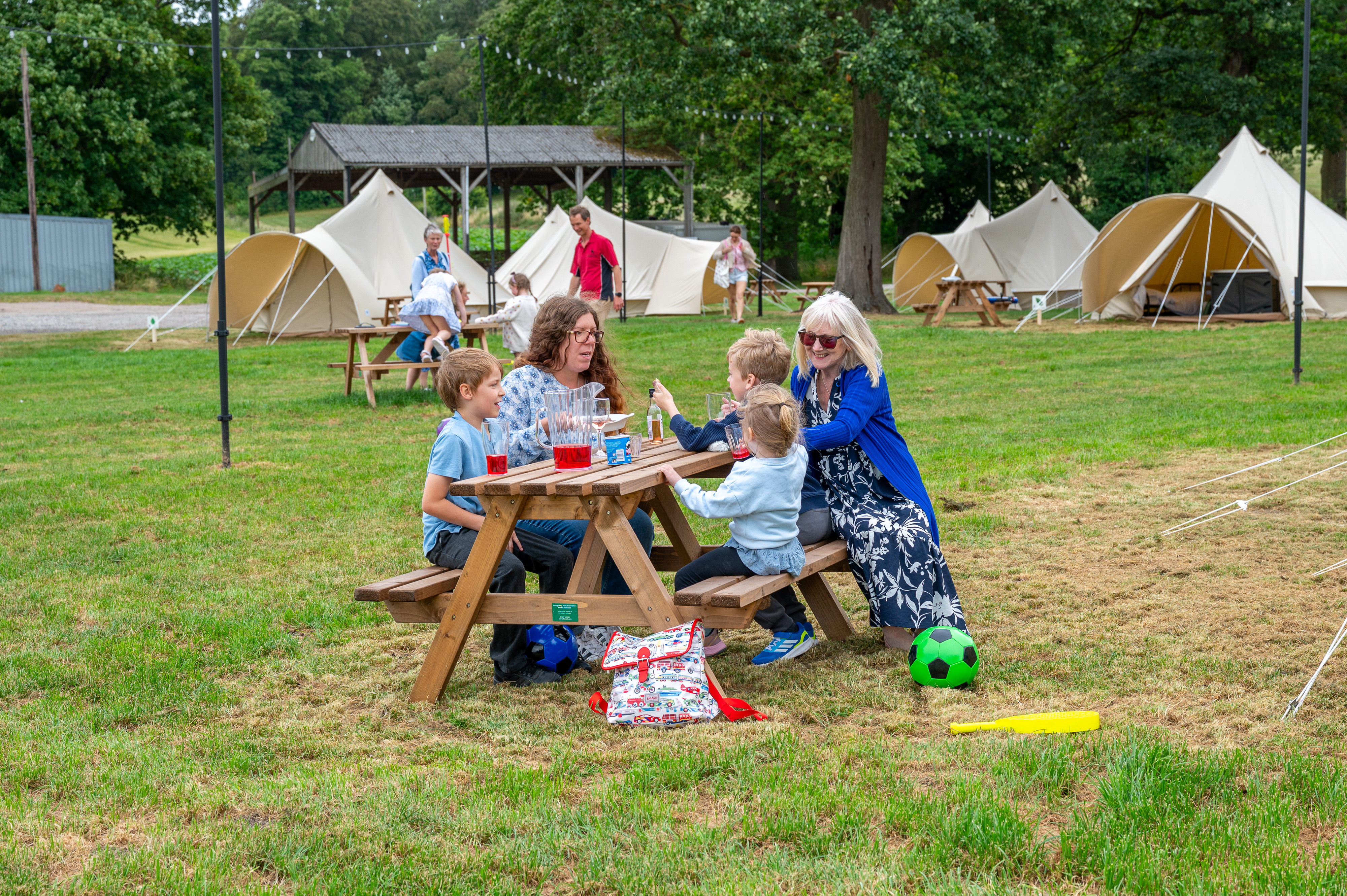 Family Sat At A Picnic Bench With Bell Tents In Background