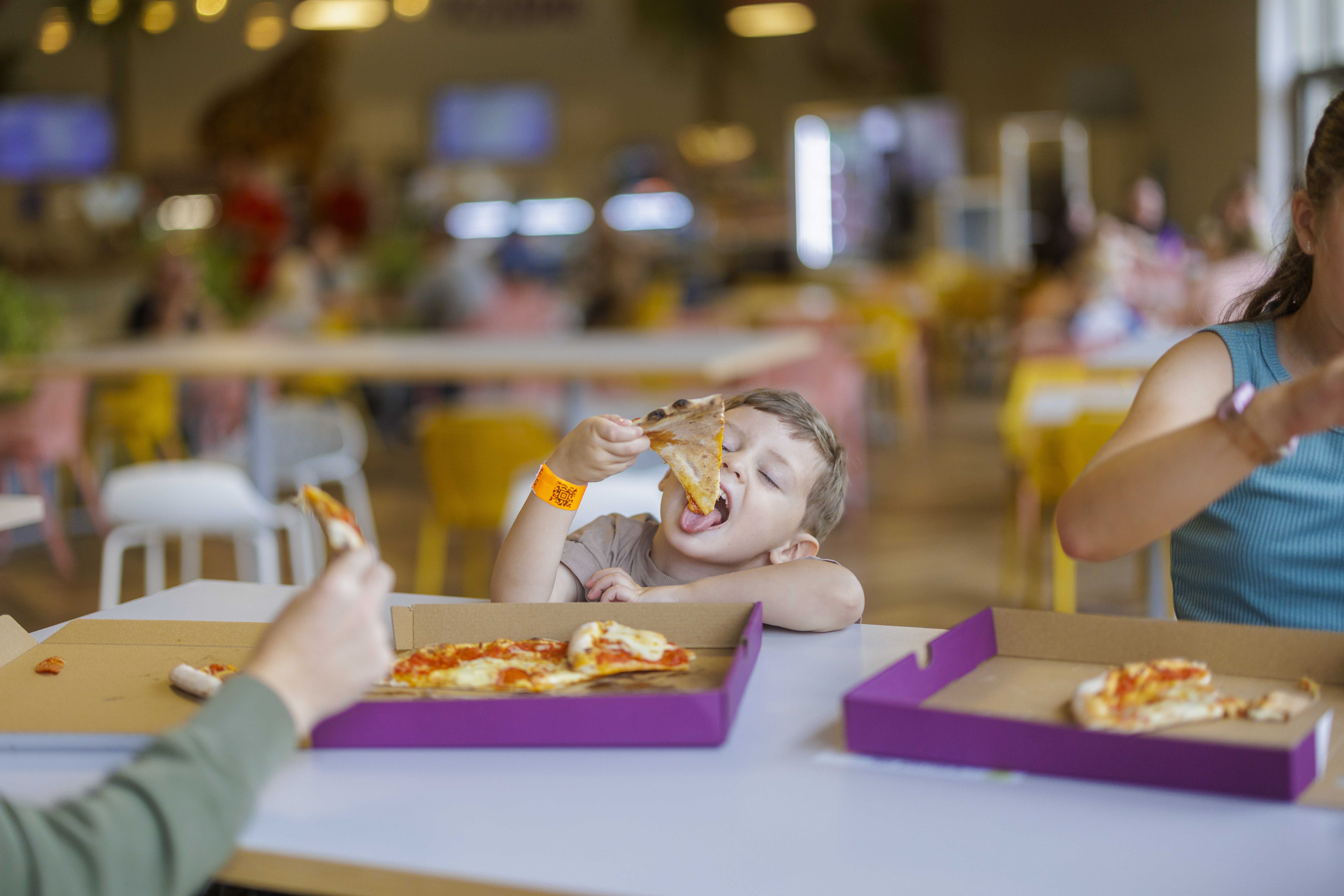 young guest holding a slice of pizza up about to take a bite in a pizzeria