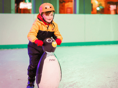 A boy learning to ice skate with a penguin aid