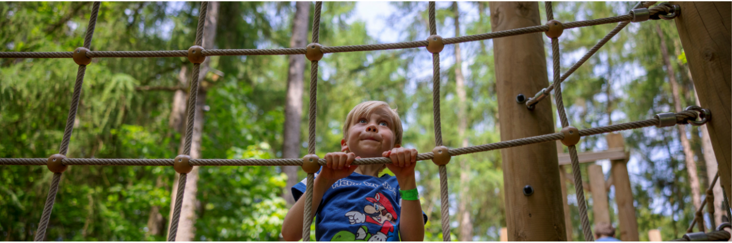 A child in a colourful outfit climbs a rope net in an outdoor playground.