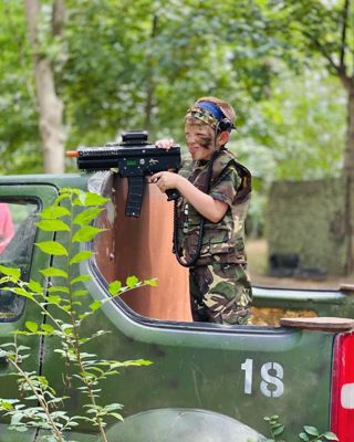 boy in camo stood on pickup truck aiming laser gun with tongue sticking out