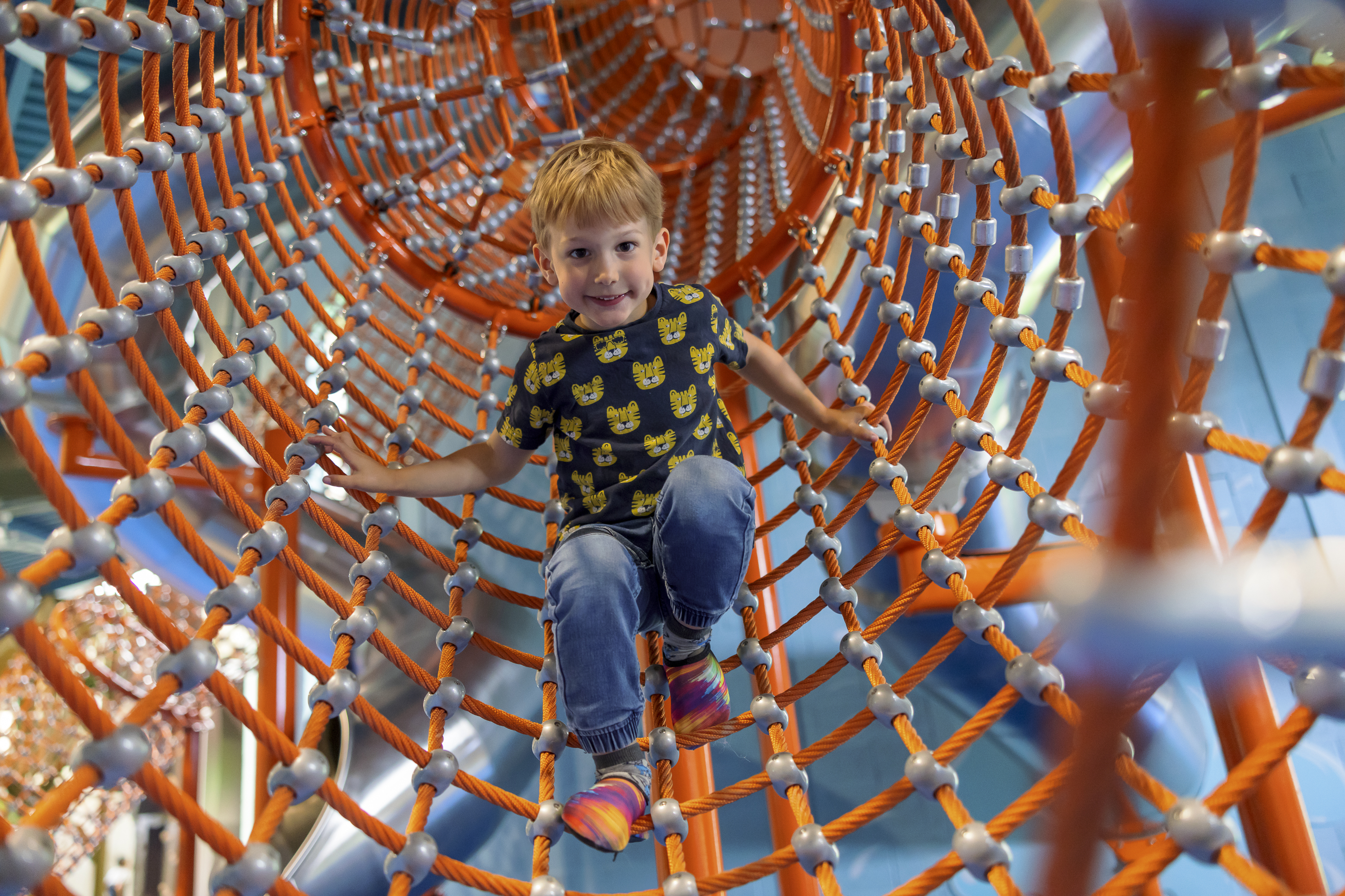 boy wearing a tshirt with tigers on climbing an orange net tunnel