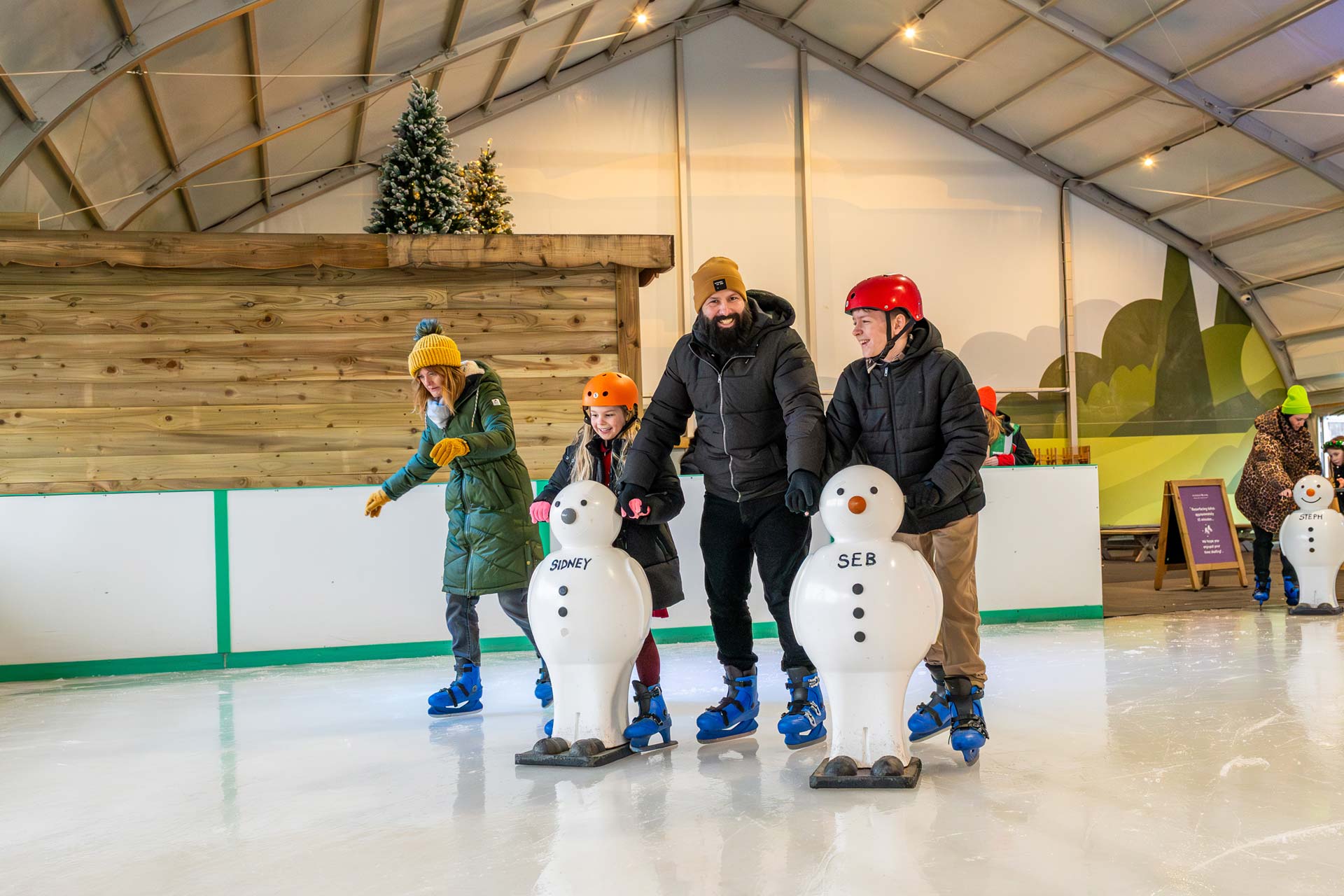 dad and two kids smiling ice skating together with snowmen skating aids