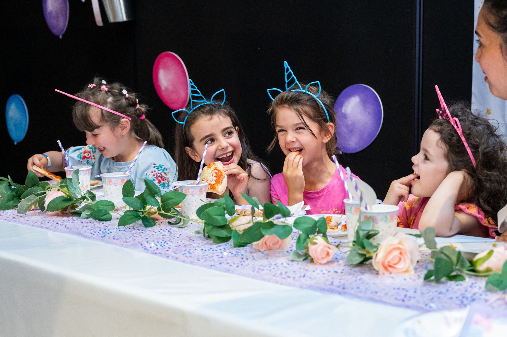 Four smiling girls sit at a table with party decorations.