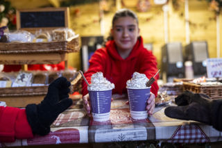 barista in red hoodie passing two hot chocolates with whipped cream to guests