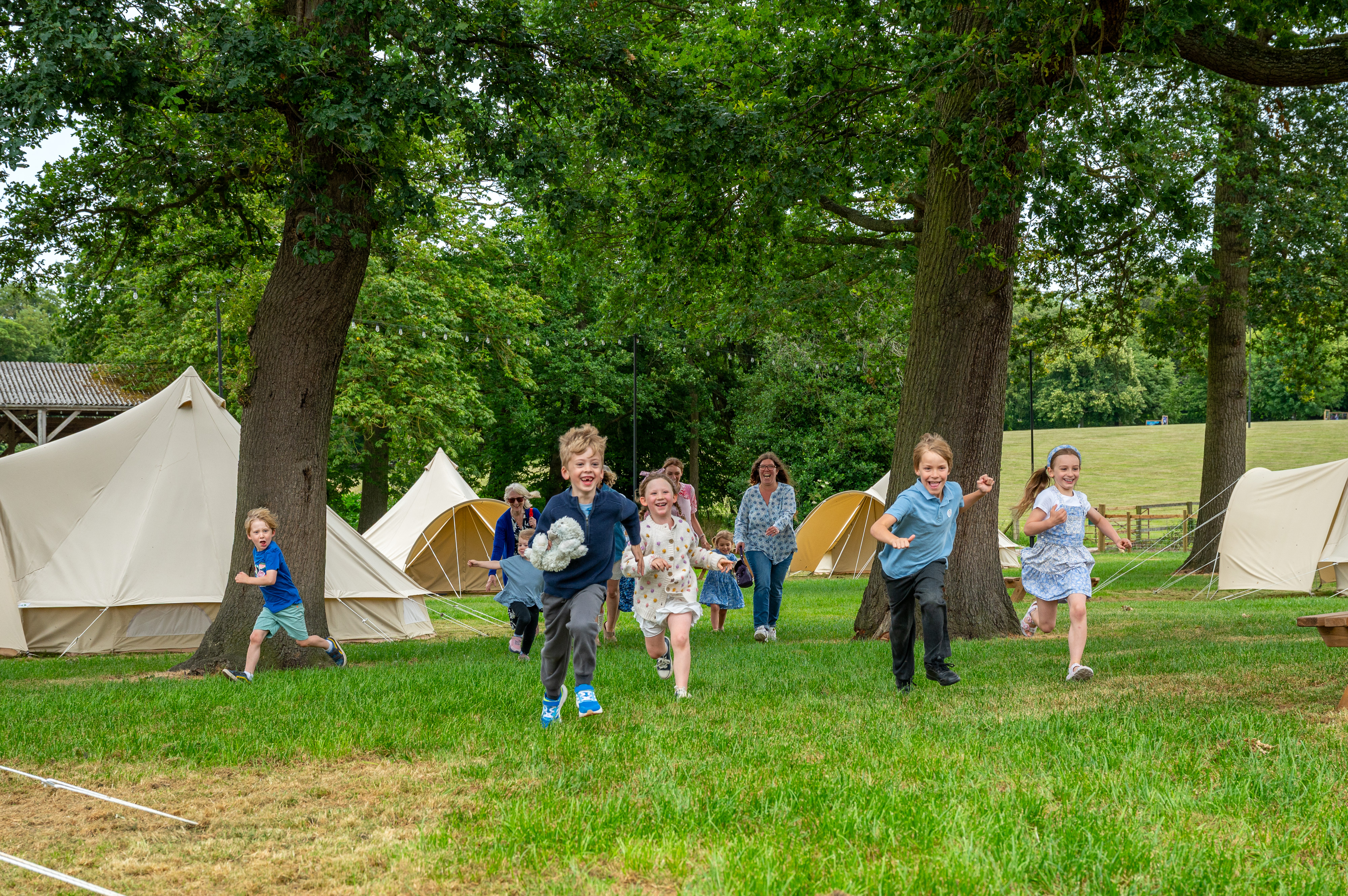 Group Of Children Running Across Campsite With Trees And Tents Behind