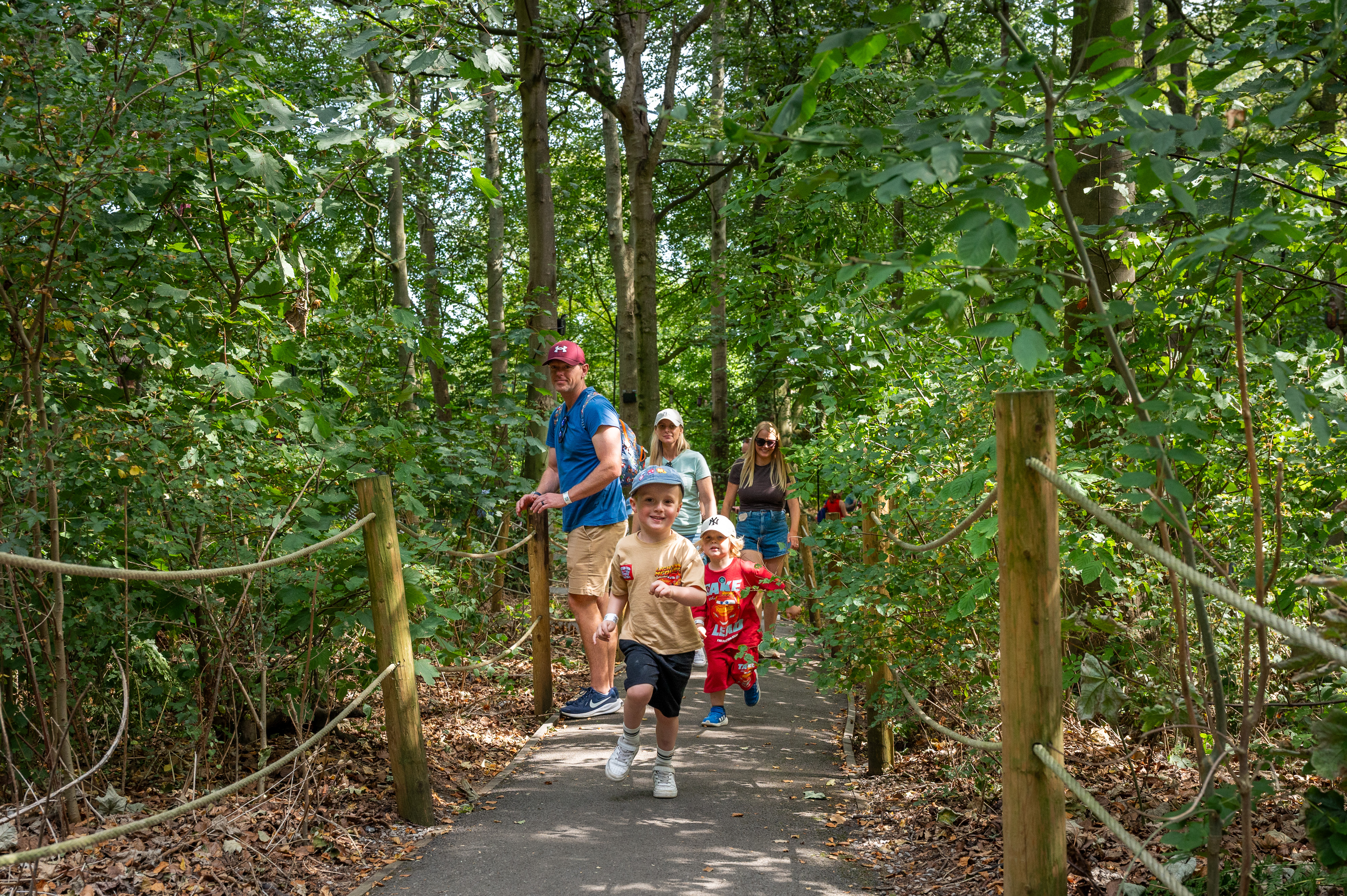boy running down path in forest with family behind