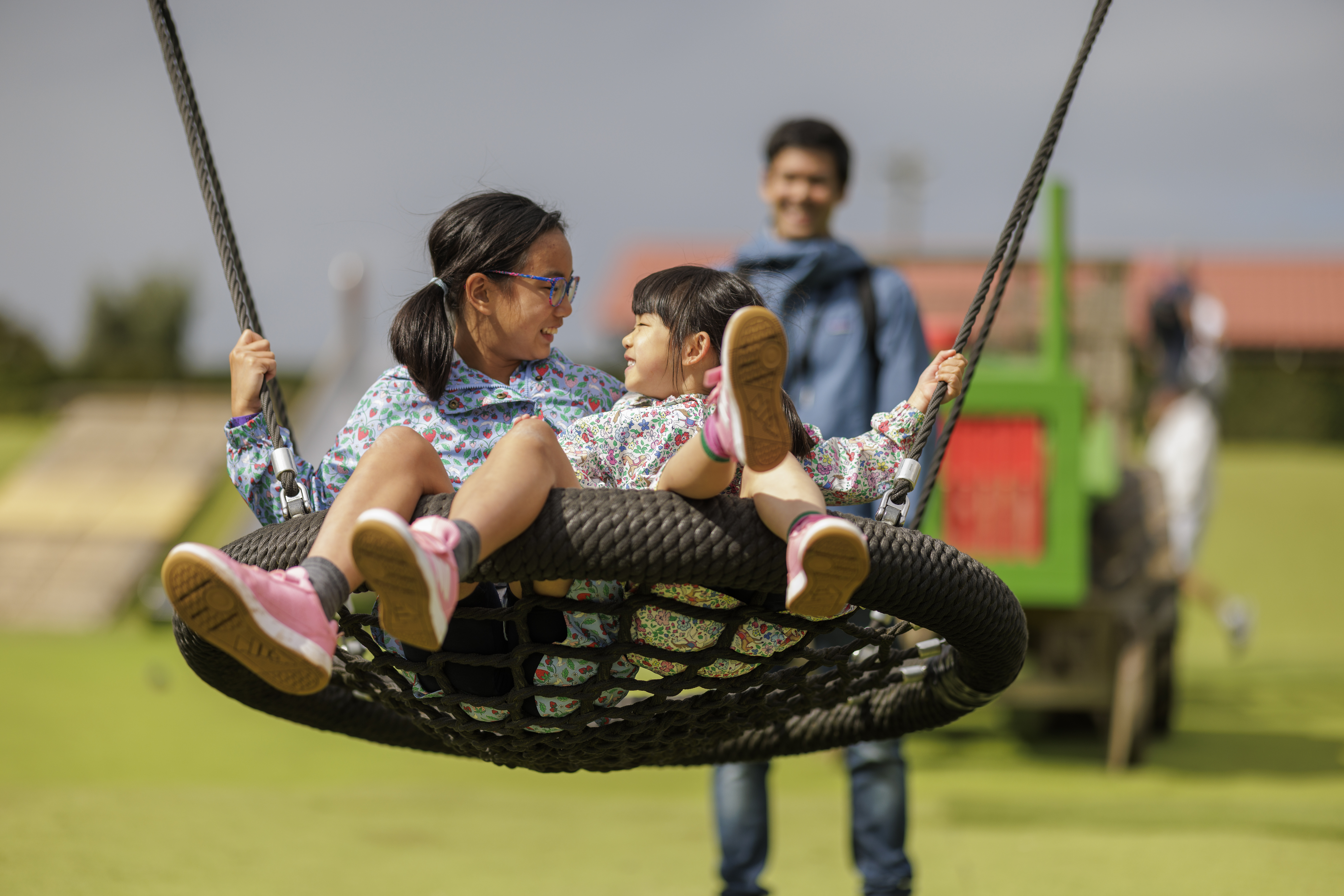 two young guests smiling at each other sitting on a swing with an adult smiling in the background
