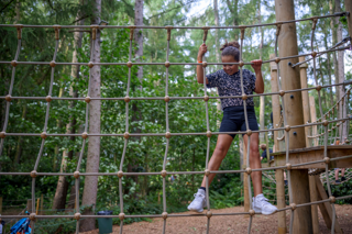 A young girl climbing on a rope net in an outdoor playground at Stockeld Park.