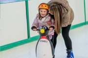 mum hugs daughter while ice skating, girl has penguin skating aid and orange helmet