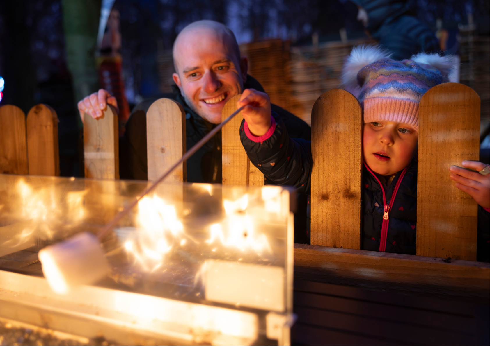 father and daughter toasting marshmallows around a fire
