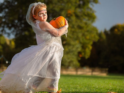 girl in halloween costume holding an orange pumpkin in a pumpkin patch