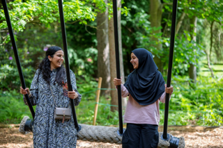 Two women swinging on a large rope swing in a lush, green forest. 