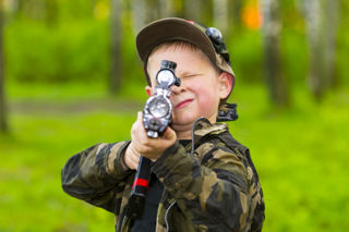 Boy with blonde hair and camo jacket aiming laser gun at camera