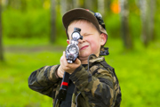 Boy with blonde hair and camo jacket aiming laser gun at camera