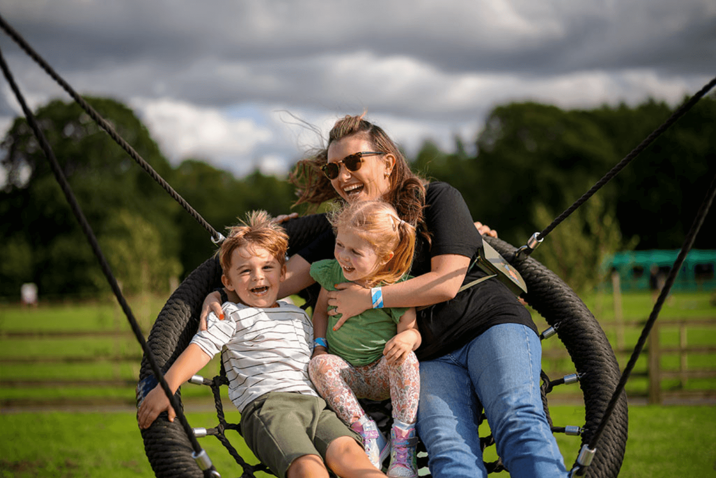 A woman and two kids swinging on a swing outside